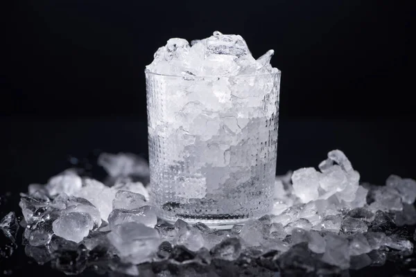 Vidro transparente preenchido com gelo quebrado isolado em preto — Fotografia de Stock