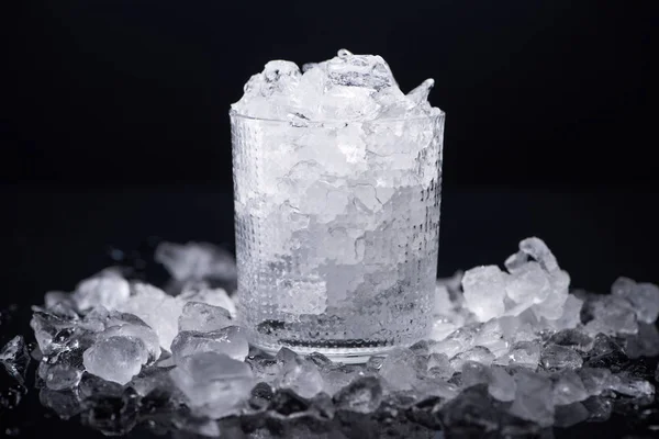 Verre transparent rempli de glace fracassée isolé sur noir — Photo de stock