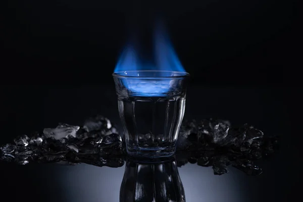 Verre transparent avec liquide brûlant près de la glace sur fond noir — Photo de stock