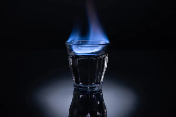 Verre transparent avec liquide brûlant sur fond noir — Photo de stock