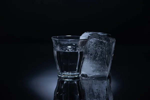 Vidro transparente com cubo de gelo e vodka sobre fundo preto — Fotografia de Stock