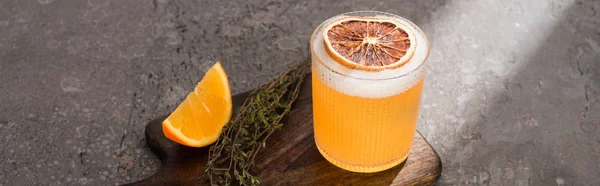 Cocktail with orange and herb on wooden cutting board on concrete surface, panoramic shot — Stock Photo