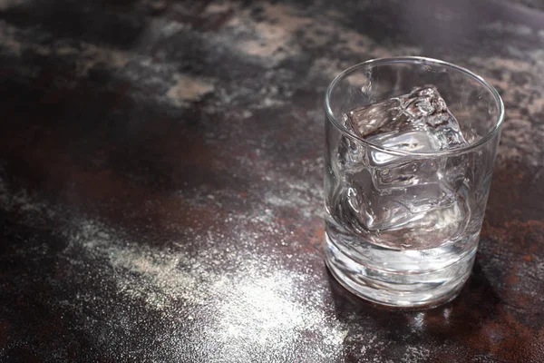 Transparent glass with ice cube and vodka on weathered surface — Stock Photo