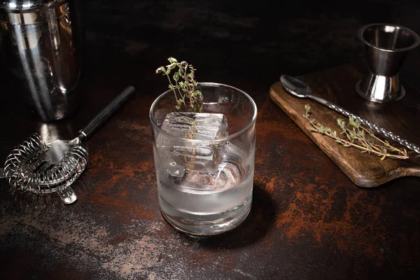 Vidrio transparente con hierbas, cubitos de hielo y vodka en la superficie erosionada - foto de stock