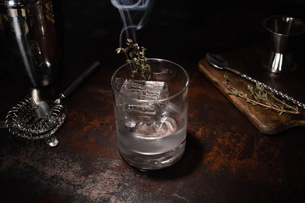 Verre transparent avec herbe brûlante, glaçon et vodka sur la surface altérée — Photo de stock