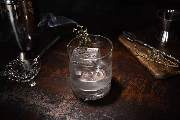 Transparent glass with burning herb, ice cube and vodka on weathered surface — Stock Photo