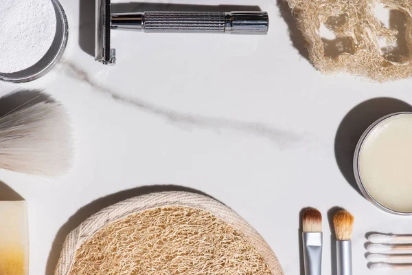 Vista dall'alto di pennelli cosmetici, rasoio, spugne, sapone, bastoncini per le orecchie, vaso di cera su sfondo bianco, concetto di zero rifiuti — Foto stock