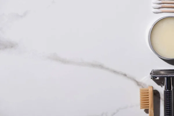 Vista superior del cepillo de dientes, maquinilla de afeitar, tarro de cera y orejeras sobre fondo blanco, concepto de cero residuos - foto de stock