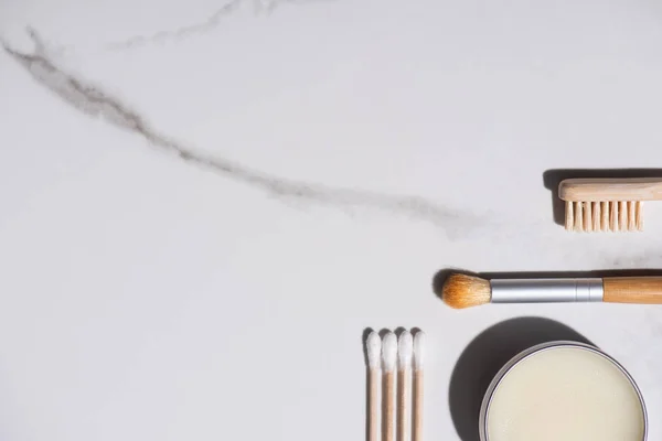 Vista superior del cepillo cosmético, cepillo de dientes, tarro de cera y orejeras sobre fondo blanco, concepto de cero residuos - foto de stock