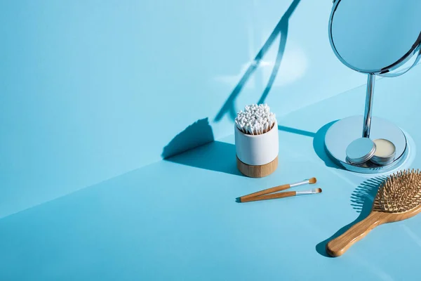 Ohrstöpsel im Zahnbürstenhalter in der Nähe von Kosmetikbürsten, Spiegel mit Wachsgefäß und Haarbürste auf blauem Hintergrund, Zero-Waste-Konzept — Stockfoto