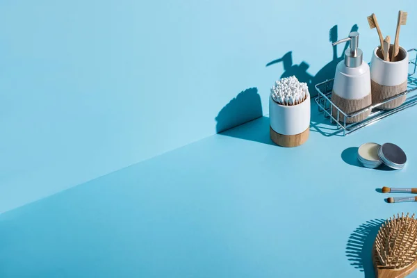 Cepillos de dientes con cepillos de dientes y orejeras, dispensador en el estante del baño, cepillos cosméticos, cepillo de pelo sobre fondo azul, concepto de cero residuos - foto de stock