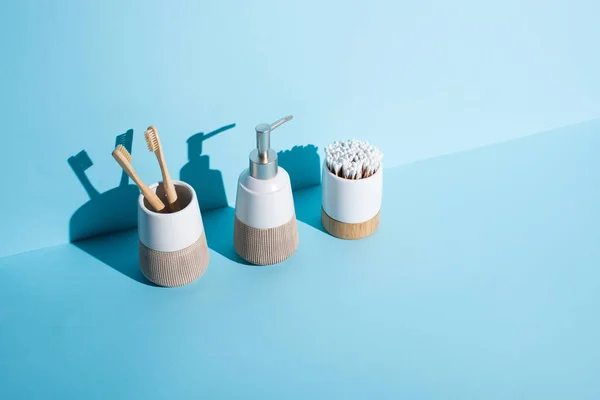 Toothbrush holders with ear sticks and toothbrushes with dispenser liquid soap on blue background, zero waste concept — Stock Photo