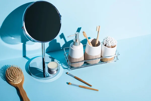 Cepillos de dientes con artículos de higiene, dispensador en el estante del baño con espejo, cepillo para el cabello, cepillos cosméticos sobre fondo azul, concepto de cero residuos - foto de stock