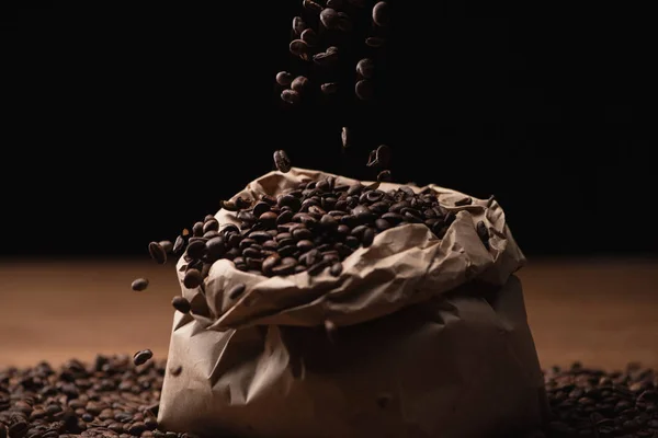 Grains de café torréfiés tombant en sac sur fond noir — Photo de stock