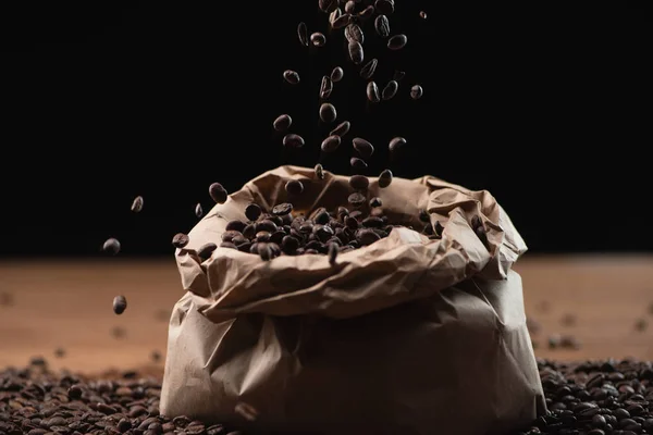 Granos de café tostados cayendo en bolsa sobre fondo negro - foto de stock