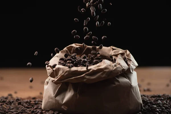 Chicchi di caffè torrefatto che cadono in borsa su sfondo nero — Foto stock