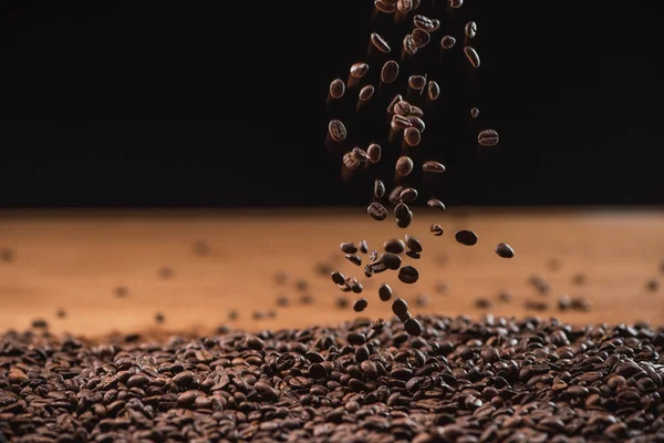 Grãos de café torrados caindo na pilha em fundo preto — Fotografia de Stock