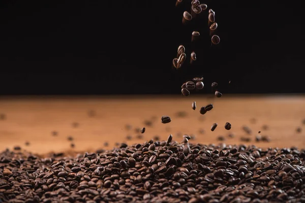 Roasted coffee beans falling on pile on black background — Stock Photo