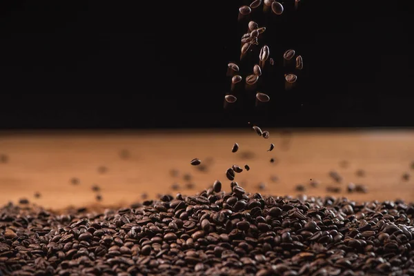 Fresh roasted coffee beans falling on pile on black background — Stock Photo