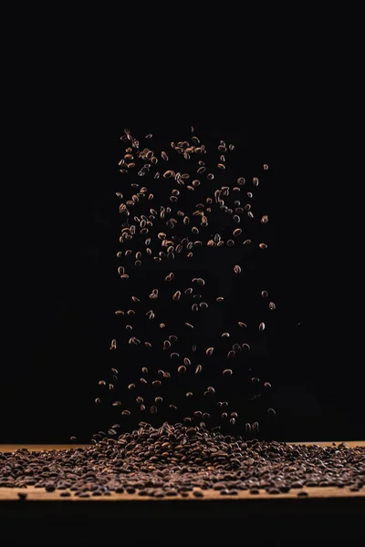 Grains de café torréfiés en pile et dans l'air isolé sur noir — Photo de stock