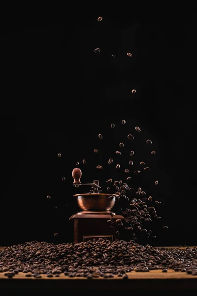Moedor de café e grãos de café torrados frescos no ar isolado em preto — Fotografia de Stock