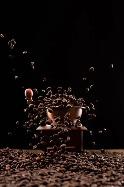 Molinillo de café y granos de café tostados frescos en el aire aislado en negro - foto de stock