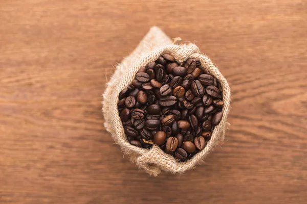 Messa a fuoco selettiva di chicchi di caffè tostato fresco a sacco sulla superficie di legno — Foto stock