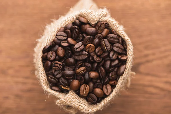 Selective focus of fresh roasted coffee beans in sack on wooden surface — Stock Photo