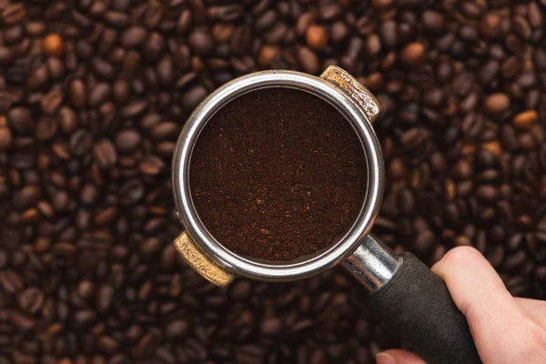 Vue recadrée de la femme tenant du café moulu dans le porte-filtre au-dessus des grains de café frais torréfiés — Photo de stock