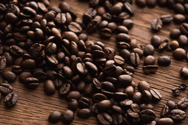 Grains de café frais torréfiés éparpillés sur une table en bois — Photo de stock