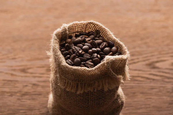 Chicchi di caffè tostato fresco a sacco sul tavolo di legno — Foto stock