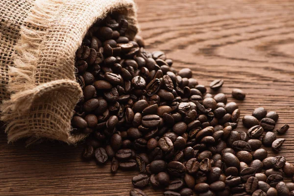 Chicchi di caffè tostati freschi sparsi dal sacco sul tavolo di legno — Stock Photo