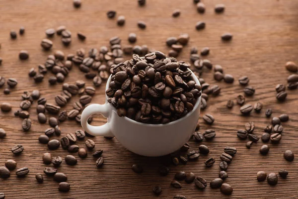 Selektiver Fokus einer Tasse frisch gerösteter Kaffeebohnen auf einem Holztisch — Stockfoto