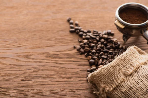 Свежий жареный кофе в зернах и молотый кофе в держатель фильтра на деревянный стол — стоковое фото