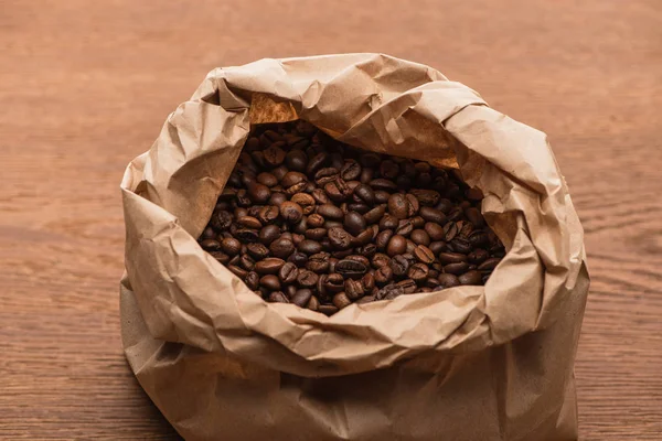 Granos de café tostados frescos en bolsa de papel sobre mesa de madera - foto de stock