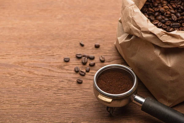 Fresh roasted coffee beans in  paper bag and ground coffee in filter holder on wooden table — Stock Photo