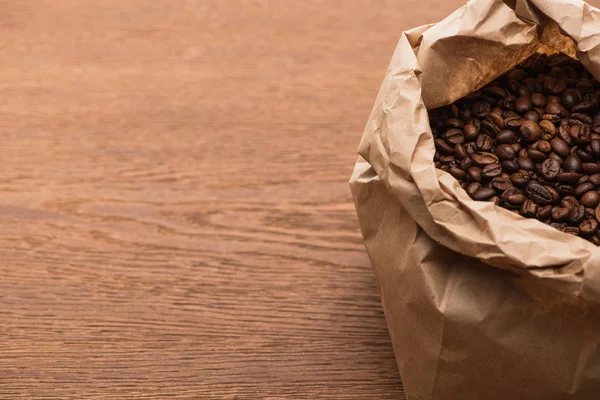 Granos de café tostados frescos en bolsa de papel sobre mesa de madera - foto de stock