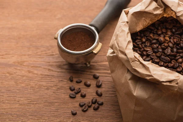 Grains de café frais torréfiés dans un sac en papier et café moulu dans un porte-filtre sur une table en bois — Photo de stock