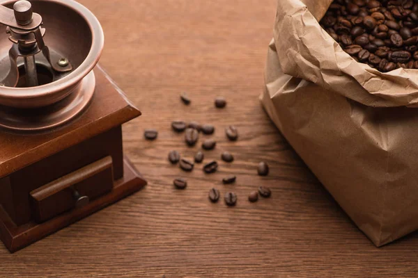Foco seletivo de grãos de café torrados frescos em saco de papel perto do moedor de café na mesa de madeira — Fotografia de Stock
