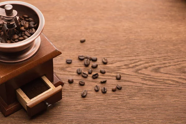 Grãos de café torrados frescos perto do moedor de café na mesa de madeira — Fotografia de Stock