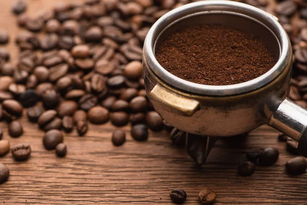 Messa a fuoco selettiva di chicchi di caffè torrefatto fresco e caffè macinato in portafiltro su tavolo in legno — Foto stock