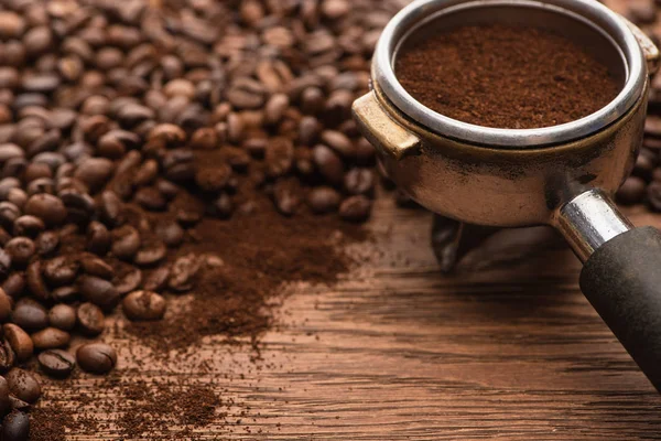 Вибірковий фокус свіжих смажених кавових зерен та меленої кави у тримачі фільтрів на дерев'яному столі — стокове фото