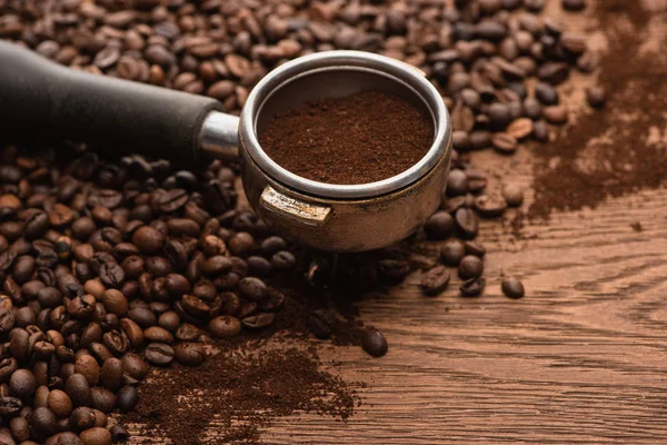 Селективный фокус свежих жареных кофейных зерен и молотого кофе в держателе фильтра на деревянном столе — стоковое фото