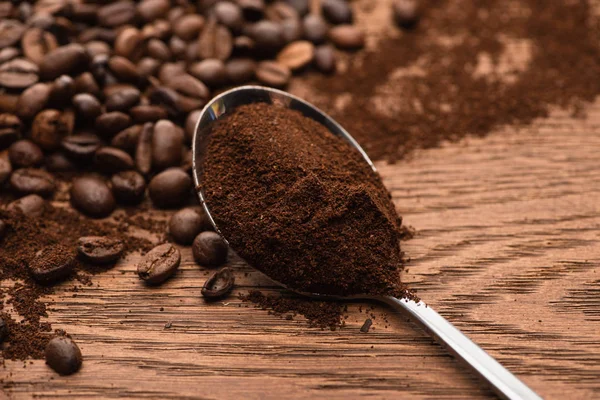 Selektiver Fokus von frisch gerösteten Kaffeebohnen und gemahlenem Kaffee im Löffel auf Holztisch — Stockfoto