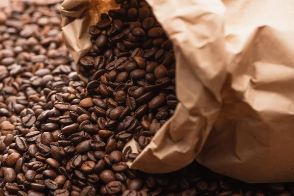 Selective focus of fresh roasted coffee beans scattered from paper bag — Stock Photo