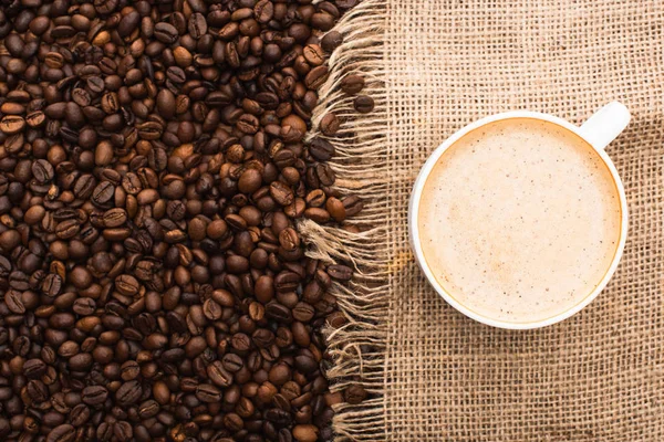 Vista superior de granos de café tostados frescos y saco con café en taza - foto de stock