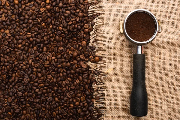 Blick von oben auf frisch geröstete Kaffeebohnen und Filterhalter mit gemahlenem Kaffee auf Sacktuch — Stockfoto