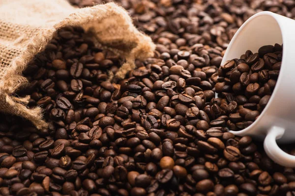 Selective focus of fresh roasted coffee beans and white cup near sack — Stock Photo