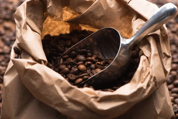 Fresh roasted coffee beans in paper bag with metal spatula — Stock Photo