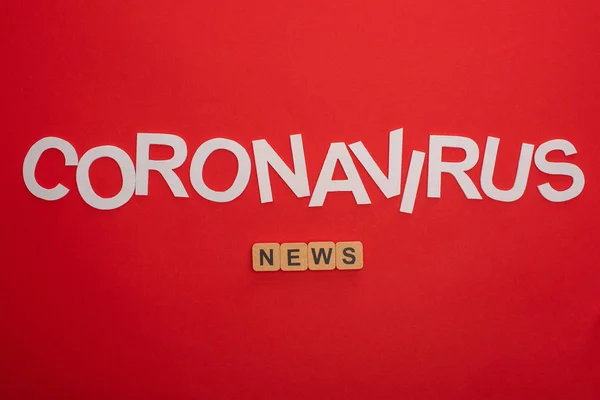 Vista superior de las letras de coronavirus y noticias de palabras en cubos de madera sobre fondo rojo - foto de stock